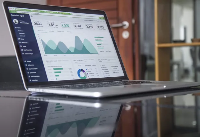 An open laptop on a glass desk showing a support dashboard with conversation volumes and response times.